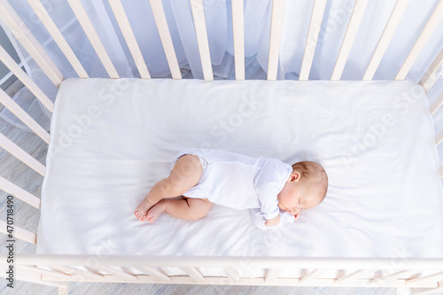 healthy sleep of a newborn baby in a cot in a bedroom on a cotton bed, top view