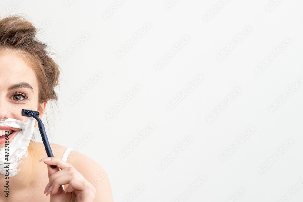Beautiful young caucasian woman shaving her face by razor on white background. Pretty smiling woman with shaving foam and razor on her face. Beautiful young caucasian woman shaving her face by razor on white background. Pretty smiling woman with shaving foam and razor on her face.