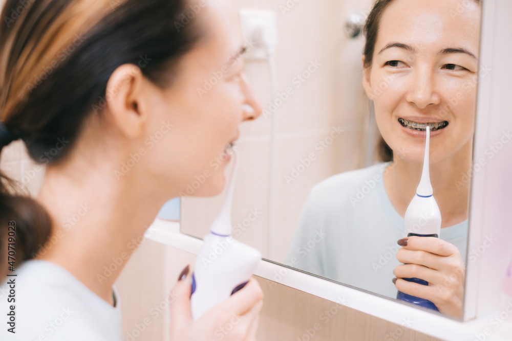Young woman with braces on her teeth brushing her teeth with by using a irrigate, before mirror. Dental and oral care. Young woman with braces on her teeth brushing her teeth with by using a irrigate, before mirror. Dental and oral care.