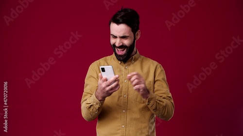 the guy looks at the phone and wins the lottery, he is very happy about this, he is black-haired, bearded, wears a brown shirt, the background is red