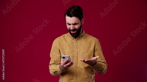 a man received a notification that he has lost everything, he does not know what to do, is disappointed, he is black-haired, bearded, wears a brown shirt, the background is red