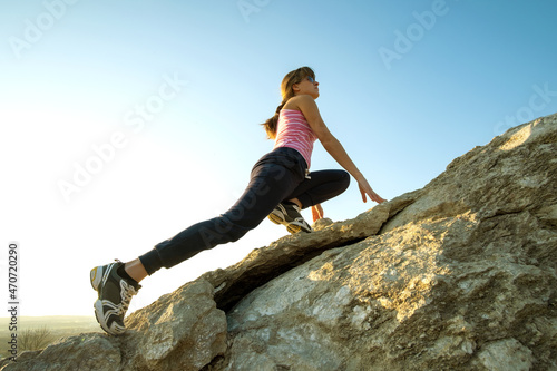 Woman hiker climbing steep big rock on a sunny day. Young female climber overcomes difficult climbing route. Active recreation in nature concept
