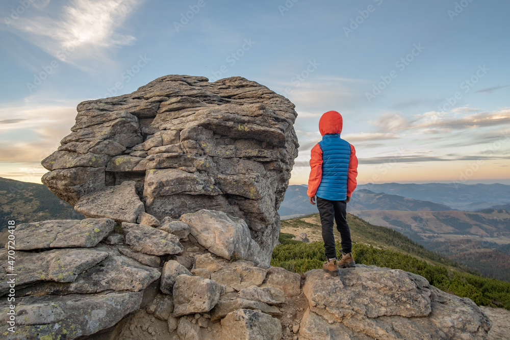 Young child boy hiker standing in mountains enjoying view of amazing mountain landscape.