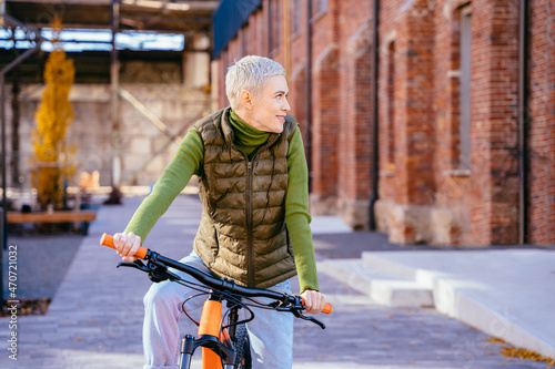 Active middle age, leisure and lifestyle concept. Portrait of mature woman 40-45 years old on bicycle. Sportive lady riding city bike in street. Smiling female cycling with her bike in autumn time out