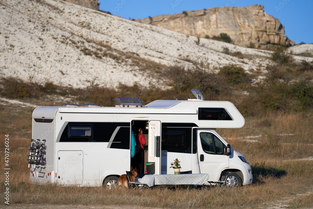 Autotourism. The caravan stopped for the night in the canyon. In front of the motorhome there is a table with a potted flower in a pot, a dog is sitting next to it. Selective focus.