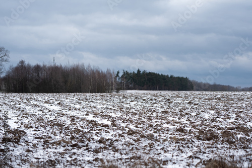 Arable fields under a thin layer of snow. Rural landscape in winter with freezing temperatures. A plowed field, prepared for the cultivation of grain.