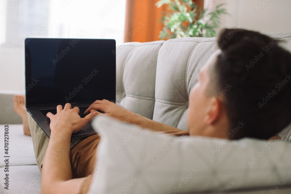 Handsome man lying on sofa and working on his laptop. Handsome man lying on sofa and working on his laptop.