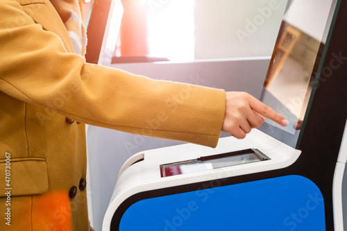 Woman passenger uses self service kiosk with touchscreen to check-in for flight to avoid long queue in contemporary airport terminal close side view photo