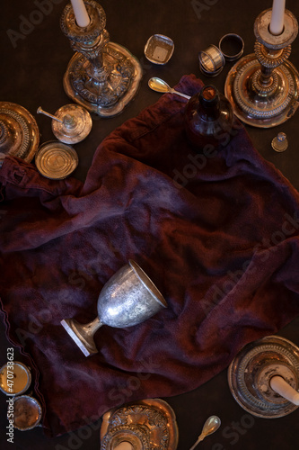 Flat lay view of tipped over silver chalice goblet grail surrounded by vintage candlesticks and miscellaneous vintage metal valuables