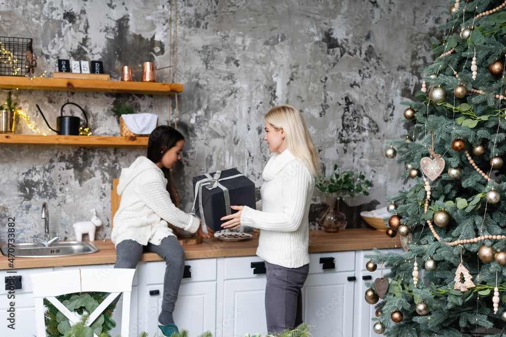 Beautiful mother and daughter have fun, hug and kiss at home near the Christmas tree in a white interior. Family happiness, holiday, joy, vacation, games with a woman. New Year's preparations Beautiful mother and daughter have fun, hug and kiss at home near the Christmas tree in a white interior. Family happiness, holiday, joy, vacation, games with a woman. New Year's preparations
