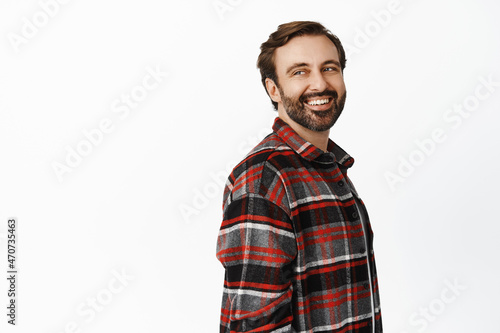 Portrait of handsome man with beard, 35 years old, looking behind at promo empty space, smiling and laughing, standing over white background