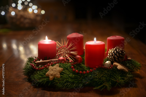 Second Advent - decorated Advent wreath from fir branches with red burning candles on a wooden table in the time before Christmas, festive bokeh in the warm dark background, copy space, selected focus