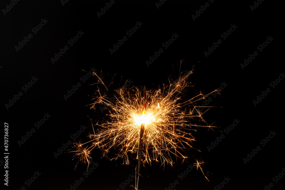 Horizontal conceptual close-up picture of an orange sparkler in action with lots of bright hot sparks flying in all directions on the black background