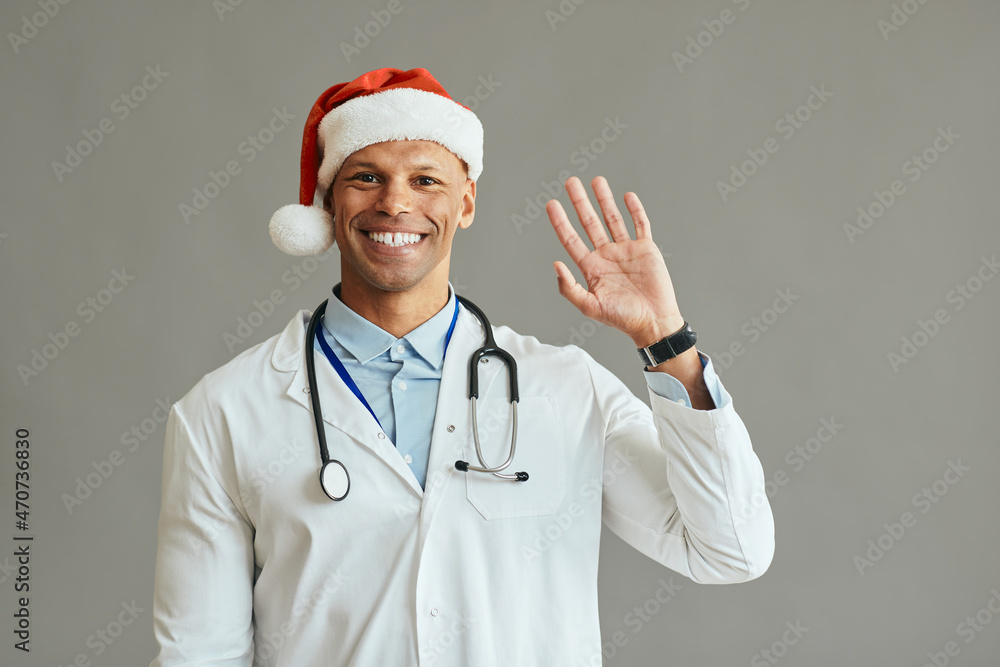 Happy African American doctor wearing Santa hat and waving to camera. Happy African American doctor wearing Santa hat and waving to camera.