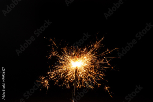 Horizontal conceptual close-up picture of an orange sparkler in action with lots of bright hot sparks flying in all directions on the black background