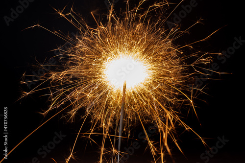 Horizontal dreamy close-up picture of a golden sparkler making many small shiny and hot sparkles on the black background