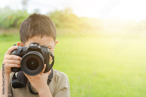 Asian boy holding a digital camera or DSLR to taking a photo with orange sunlight background. photo