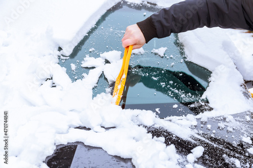 A car covered with snow. A man cleans the car from the snow with his hand with special brushes.
