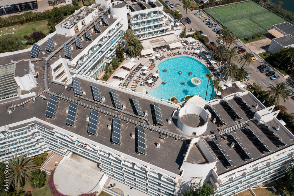 Aerial drone photo taken on the beautiful island of Majorca in Spain showing a top down view of a hotel building apartment with solar panels on the roof and and an out door swimming pool in the summer