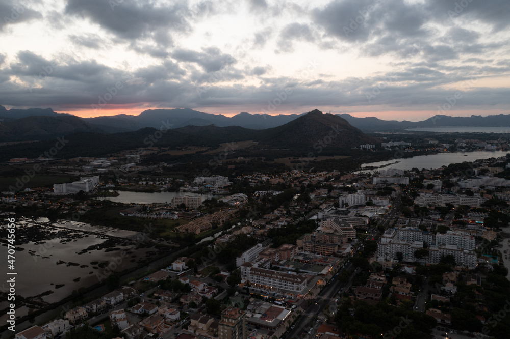 Aerial drone photo taken on the beautiful island of Majorca in Spain showing the main town centre at night time with the sun setting over the mountains