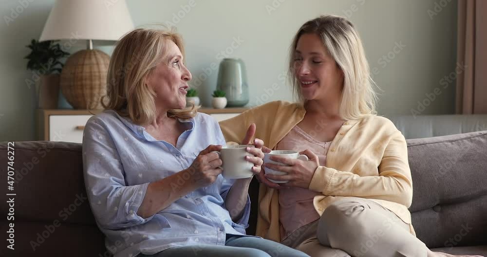 Mature mother grown up daughter good friends sit on sofa talk chat discuss positive news hold cups of coffee tea. Smiling aged single mom enjoy visit of adult child laugh hold pleasant conversation Mature mother grown up daughter good friends sit on sofa talk chat discuss positive news hold cups of coffee tea. Smiling aged single mom enjoy visit of adult child laugh hold pleasant conversation