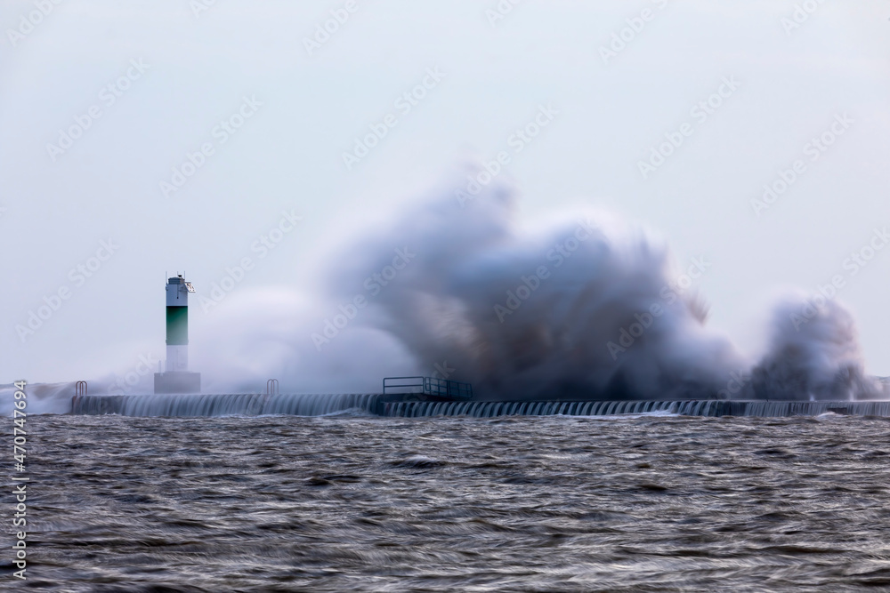The waves crashing on a pier with a lighthouse on lake Michigan