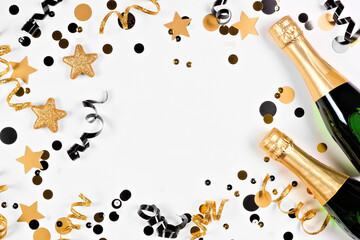 New Years Eve frame of gold and black confetti, streamers and champagne. Top view over a white background.