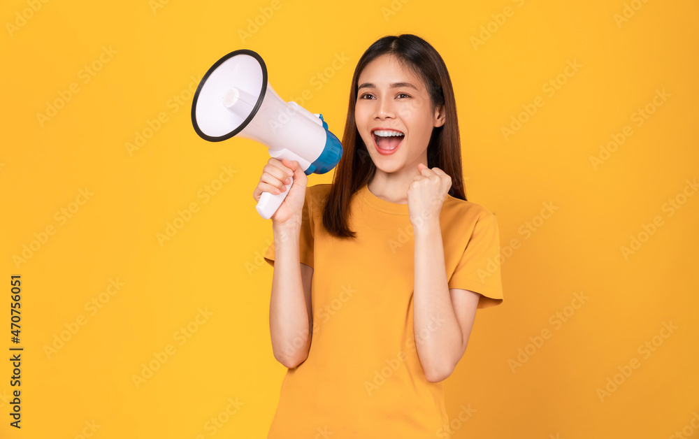 Smile Asian woman holding megaphone with fists clenched celebrating victory expressing success on yellow background. Smile Asian woman holding megaphone with fists clenched celebrating victory expressing success on yellow background.