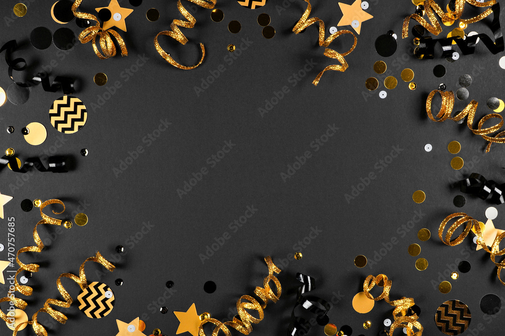 New Years Eve frame of glittery gold stars, streamers, decorations and  noisemakers. Above view on a black background. Stock Photo
