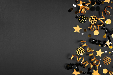 New Years party side border with glittery black and gold streamers and confetti. Top view on a black background.