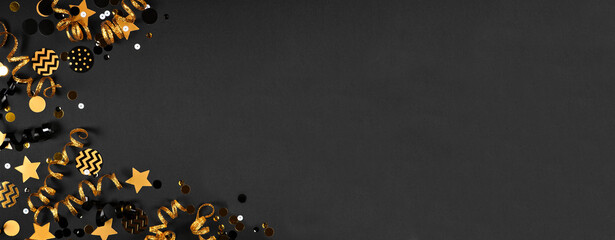 New Years party frame of glittery black and gold streamers and confetti. Above view on a black background.