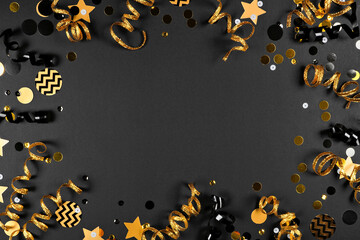 New Years party frame of shiny black and gold black and gold streamers and confetti. Top down view on a black background.