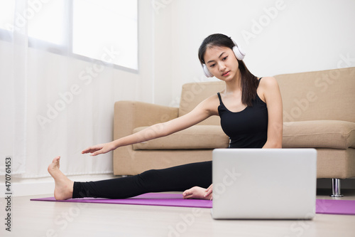 Young asian sport woman sitting practicing yoga lesson. Stretching leg training workout at home for good health and body shape. Learning skill form video online class by laptop.