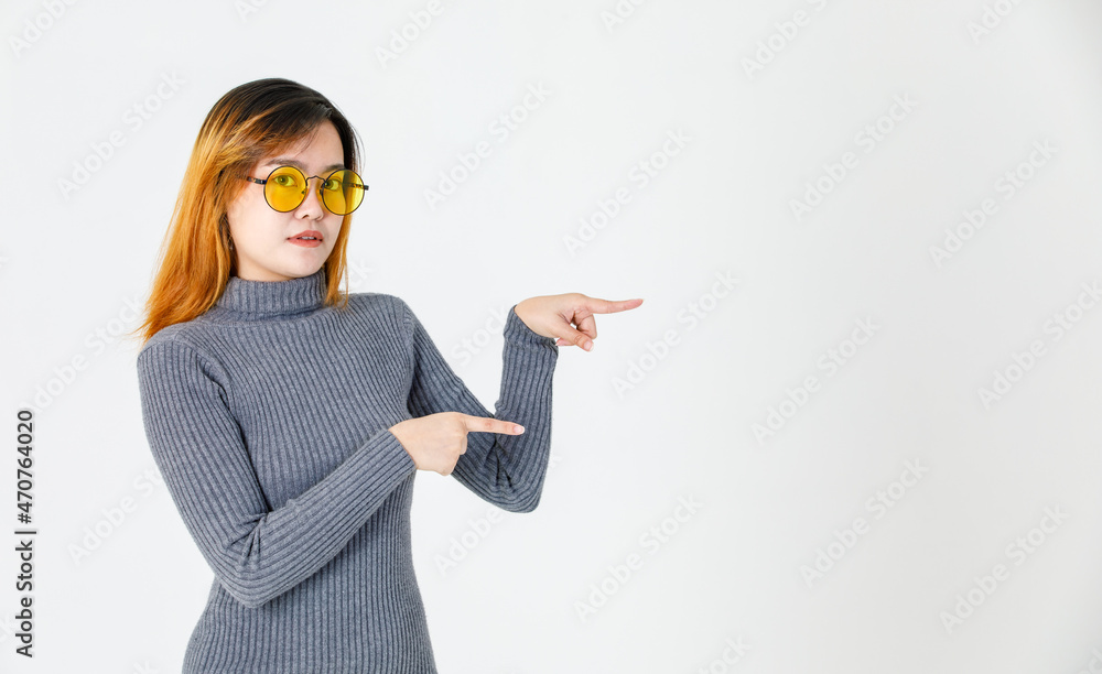 Asian young female model in gray turtleneck sweater and orange lens sunglasses standing pointing index fingers to empty copy space presenting promoting product on white background Asian young female model in gray turtleneck sweater and orange lens sunglasses standing pointing index fingers to empty copy space presenting promoting product on white background