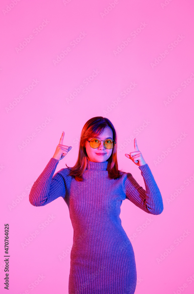 Studio shot Asian young female model in gray turtleneck sweater and orange lens sunglasses standing pointing index fingers to empty copy space presenting promoting product on pink light background Studio shot Asian young female model in gray turtleneck sweater and orange lens sunglasses standing pointing index fingers to empty copy space presenting promoting product on pink light background