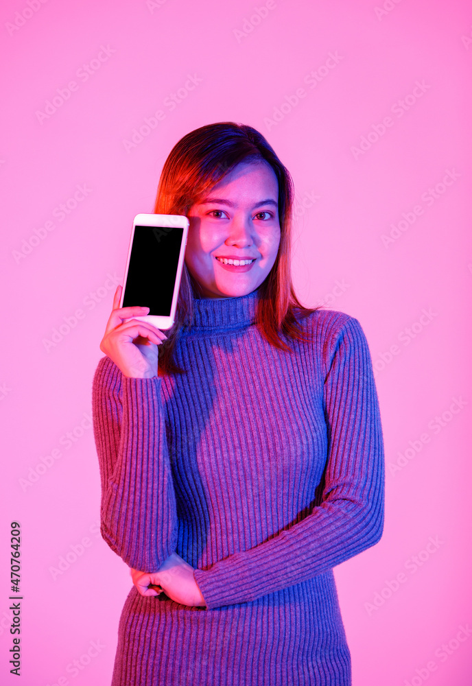 Closeup studio shot of empty black blank screen touchscreen smartphone for advertising in Asian young female model in gray turtle neck sweater hand look at camera on pink light blurred background Closeup studio shot of empty black blank screen touchscreen smartphone for advertising in Asian young female model in gray turtle neck sweater hand look at camera on pink light blurred background