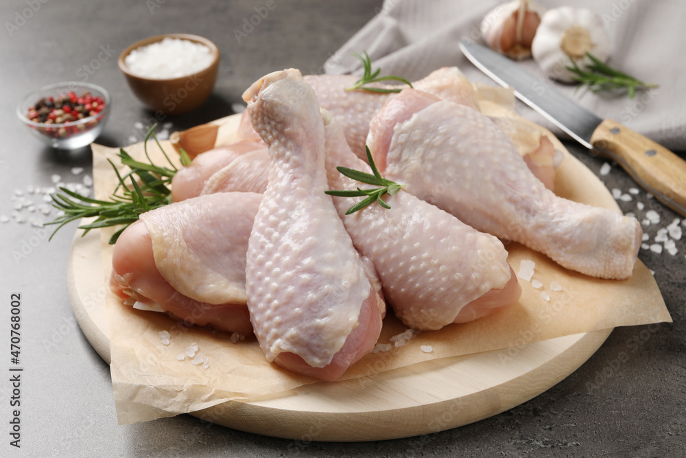 Wooden board with fresh raw chicken legs and other products on grey table