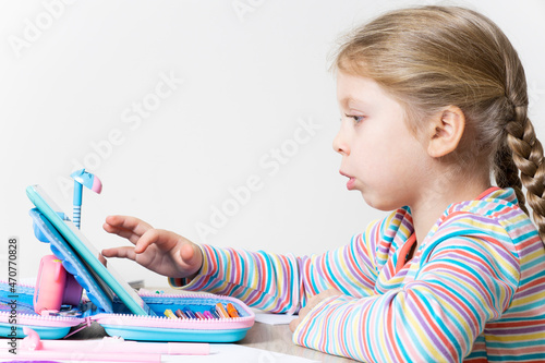 The girl is engaged in online education on the tablet at the table in the children's room. Child and gadget. Watching cartoons, reading, chatting, listening to music, playing on your tablet