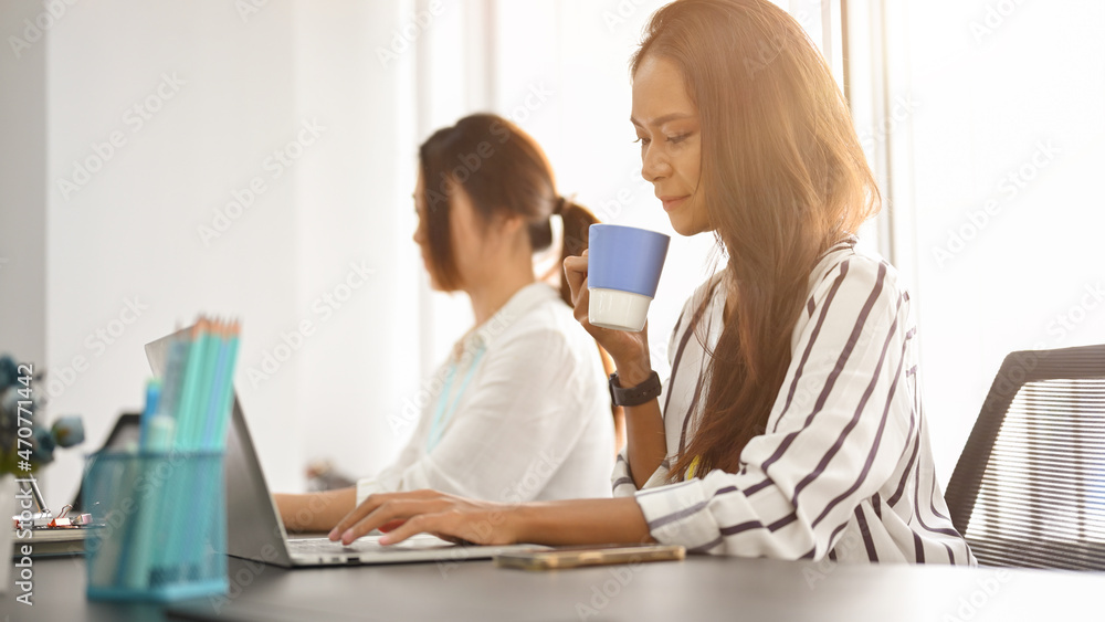 Female employees working on laptop while drinking a morning hot tea Female employees working on laptop while drinking a morning hot tea
