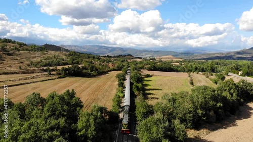 Aerial: old diesel train traveling along fields under summer blue sky with some clouds on a sunny day photo