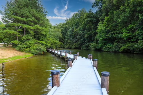 a gorgeous day at the still lake with a long brown and gray wooden boat dock out over the lake surrounded by lush green trees with blue sky and clouds at Lake Kedron in Peachtree City, Georgia USA photo