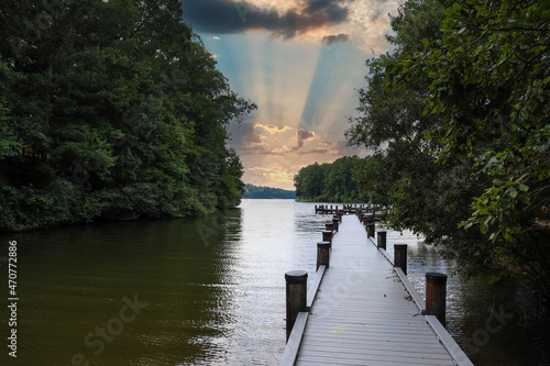 a gorgeous shot of the still blue lake water with a wooden dock over the water surrounded by lush green trees with powerful clouds at sunset at Lake Kedron in Peachtree City, Georgia USA photo