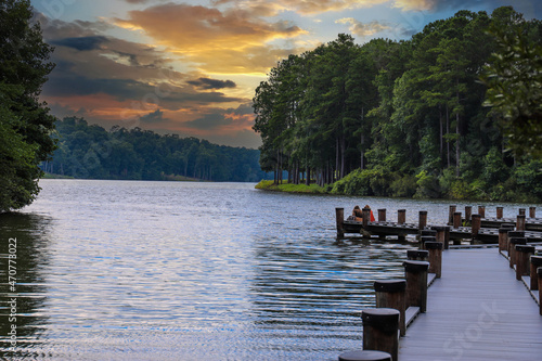 a gorgeous shot of the still blue lake water with a wooden dock over the water surrounded by lush green trees with powerful clouds at sunset at Lake Kedron in Peachtree City Georgia USA photo