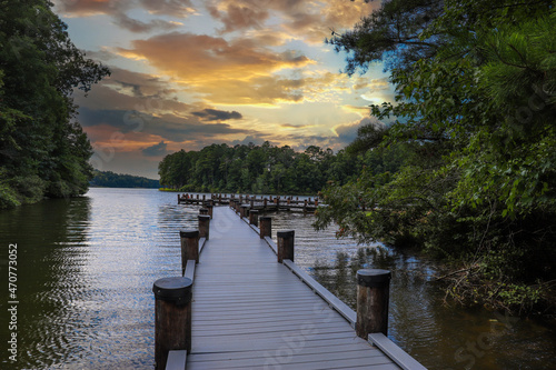 a gorgeous shot of the still blue lake water with a wooden dock over the water surrounded by lush green trees with powerful clouds at sunset at Lake Kedron in Peachtree City, Georgia USA photo