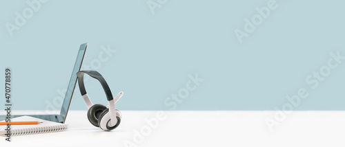 Side view of slim laptop with headphones headset on white desk. Mockup screen. Distant learning. working from home, online courses or support. Audio podcast. Helpdesk or call center banner photo