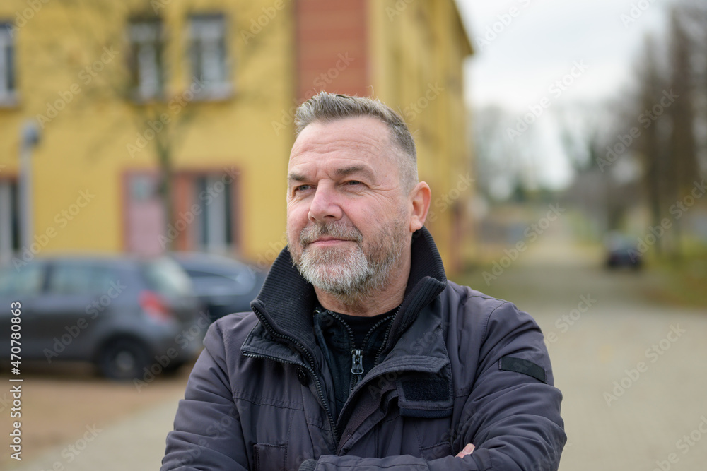 Middle-aged bearded man standing with folded arms in street Middle-aged bearded man standing with folded arms in street