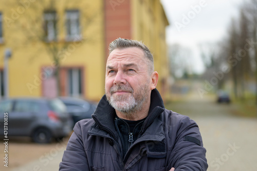Middle-aged bearded man standing with folded arms in street
