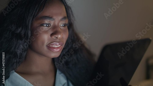 Shocking content. Young amazed african american woman surfing on digital tablet online, reading breaking news in night photo