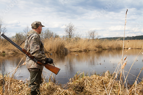 the hunter stands on the shore of the lake and looks at the duck decoys photo