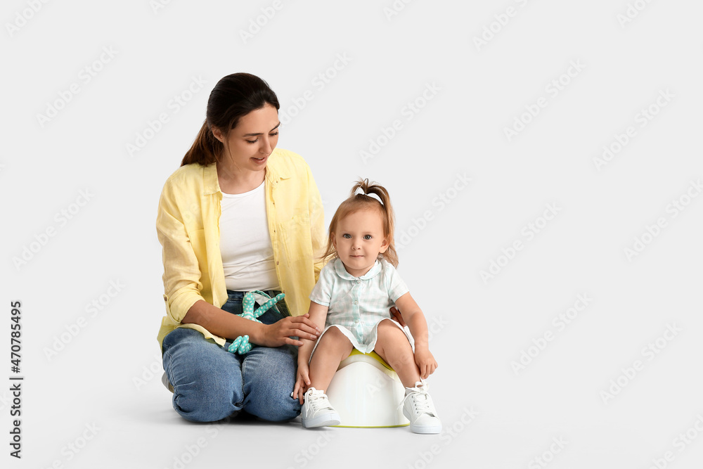 Mother potty training her little daughter on light background Mother potty training her little daughter on light background